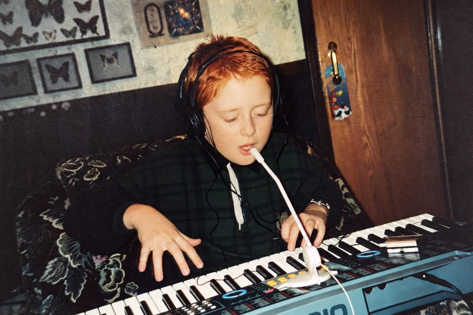 Childhood photograph of Nik McFly wearing headphones at a keyboard at home